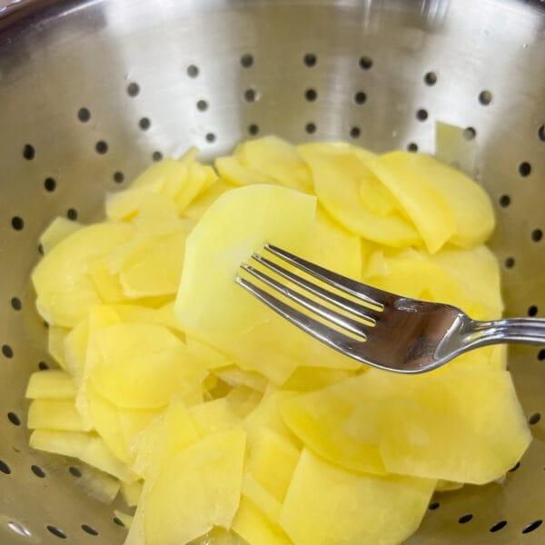 fork in blanched potato slice over colander