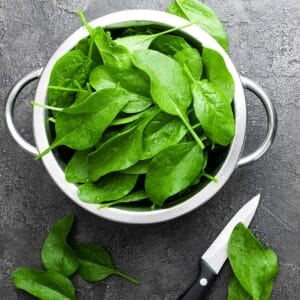 fresh spinach in colander on gray counter with knife