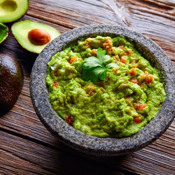 guacamole with tomatoes and cilantro in mortar with avocado beside