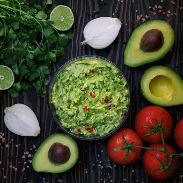 bowl of guacamole with ingredients surrounding it on dark