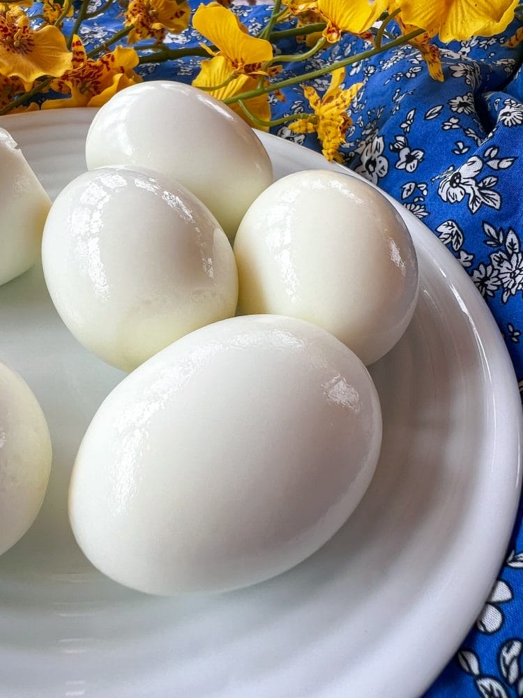 6 boiled and peeled eggs on a plate with blue tablecloth in the background