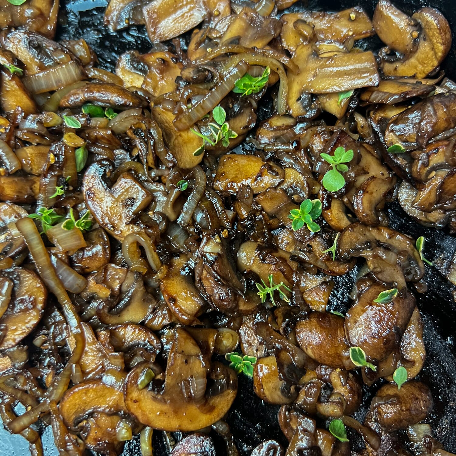 sauteed mushrooms and onions in pan coated with sauce and sprinkled with herbs