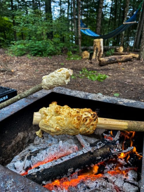 two sticks with bannock over campfire coals