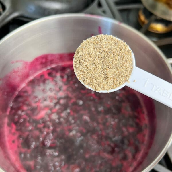 ground chia seed in measuring spoon over pot of bubbling blueberries
