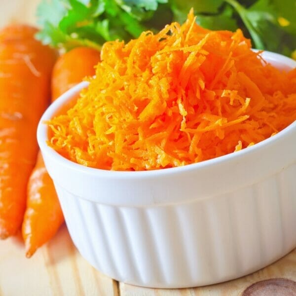 raw shredded carrots in bowl with carrots beside it