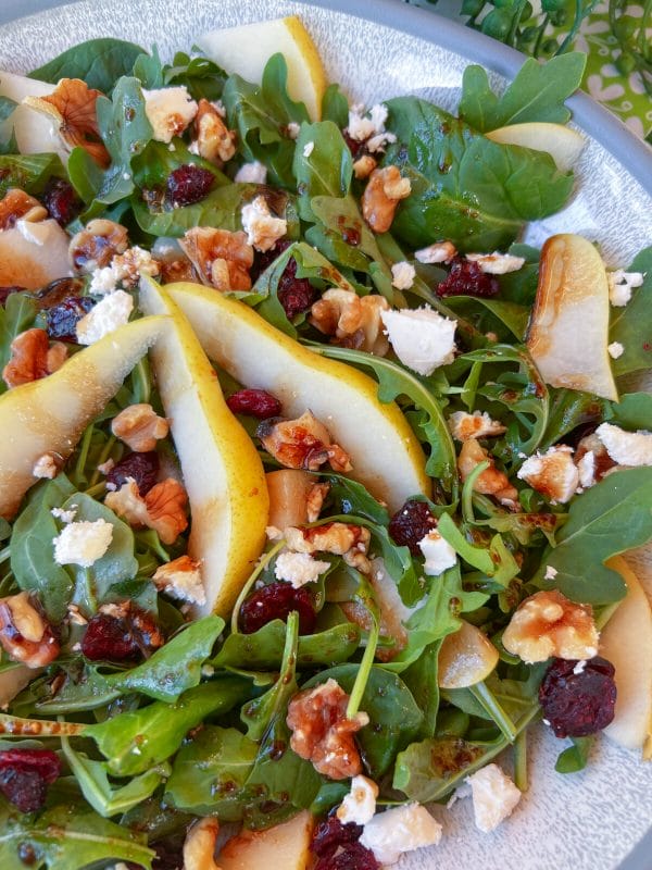 sliced pears on arugula in bowl with cranberries, walnuts and feta