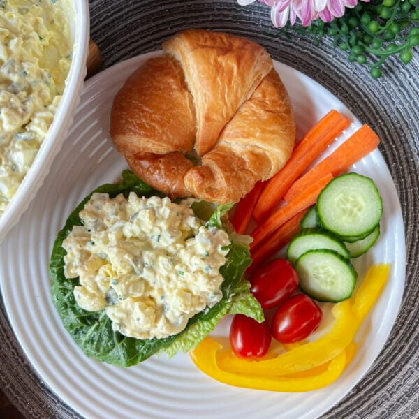 Egg salad on croissant with cut veggies on plate