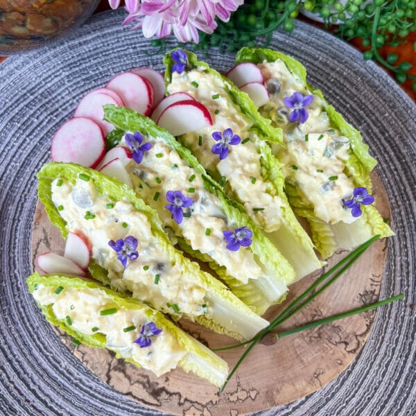 egg salad in small lettuce cups with chives and radishes on a round board