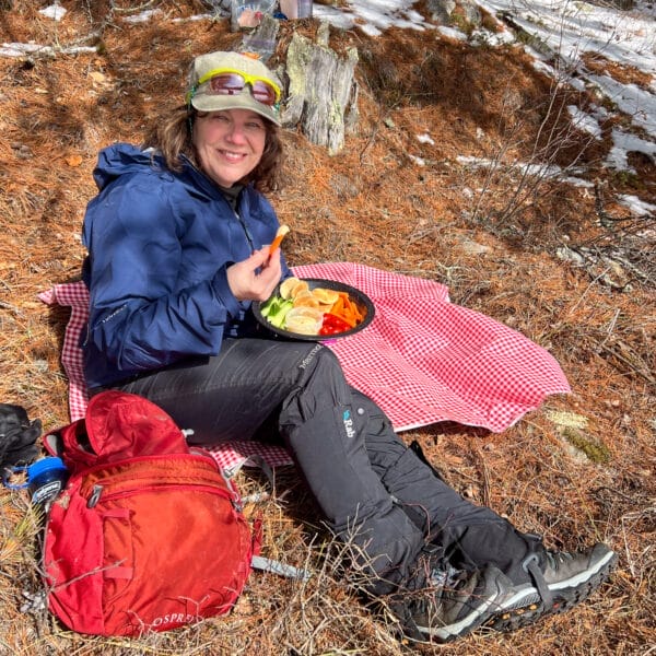 Getty sitting on picnic blanket in woods with snow eating hummus