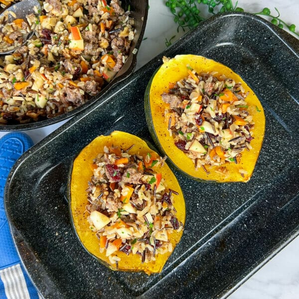 two stuffed acorn squash in baking dish with extra stuffing
