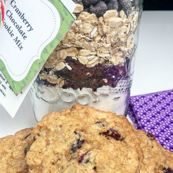 Jar of cranberry oat cookie mix with gift tag and instructions. Prepared cookies shown in front.