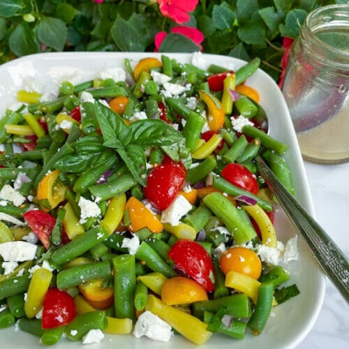 close up green bean salad, including tomatoes, beans, feta, basil leaves
