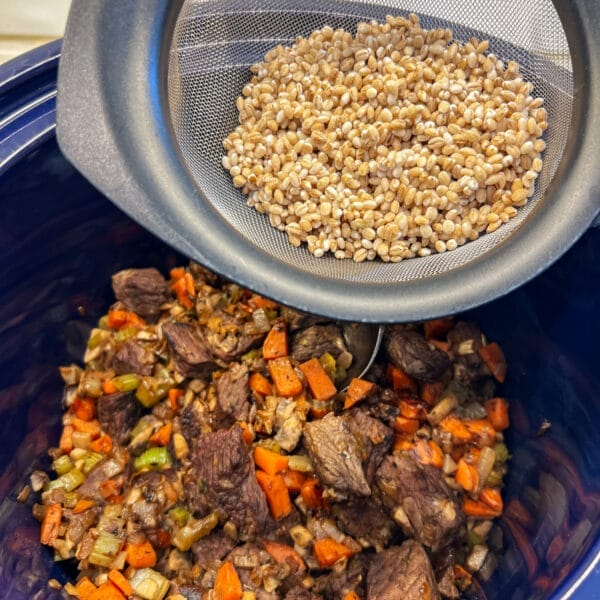 barley in strainer over crockpot with browned veggies and meat