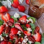 strawberry spinach salad with pecans on plate with dressing next to it