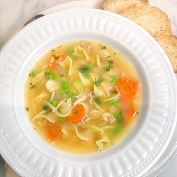 chicken noodle soup in white rimmed bowl showing wide noodles and veggies