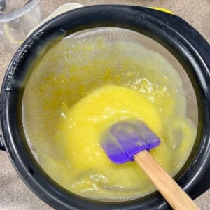 rubber spatula in curd in  strainer showing bits of zest