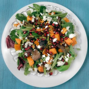 Butternut squash and feta and pomegranates on greens on plate blue background