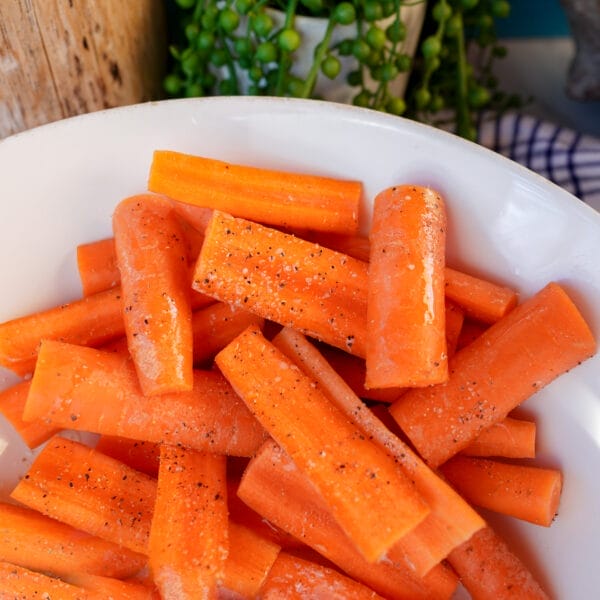carrot spears in white bowl tossed with oil and seasoning