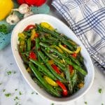 green beans and sweet peppers with bits of garlic on serving plate with parsley garnish