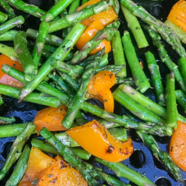 asparagus pieces and orange sweet pepper pieces in grilling basket on bbq