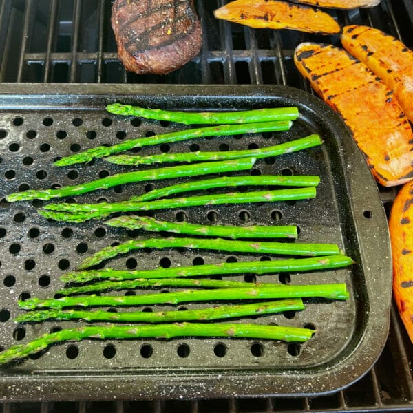 asparagus spears on grill pan on bbq with steak and sweet potatoes