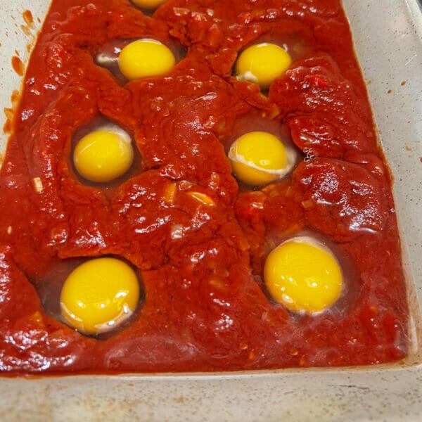 raw eggs nestled in tomato sauce in casserole dish