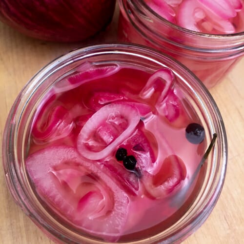 close up of red pickled onions and spices in a canning jar, no lid