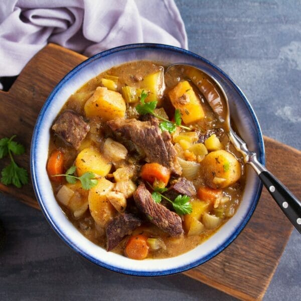 bowl of stew showing potatoes, meat, carrots and springs of parsley
