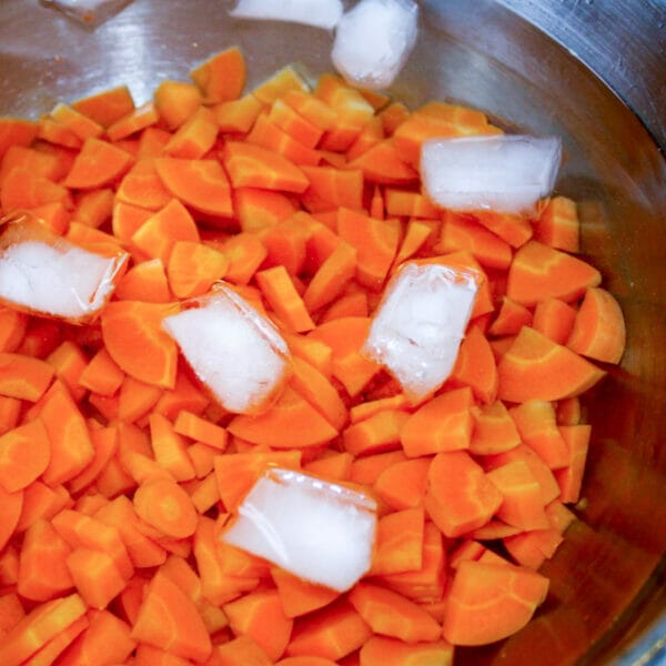blanched sliced carrots in water with ice cubes