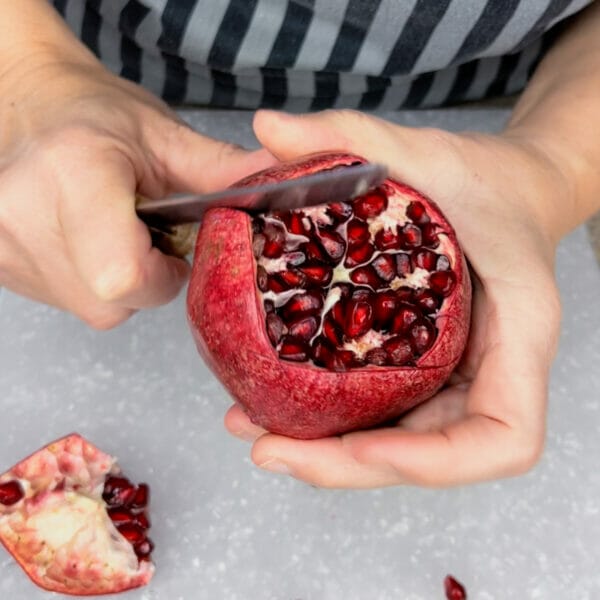 hand cutting into side of pomegranate following white pith line