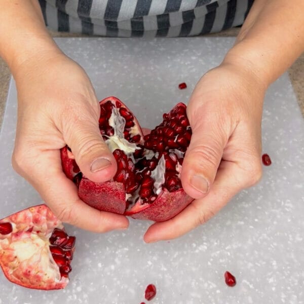 two hands splitting pomegranate to expose inside
