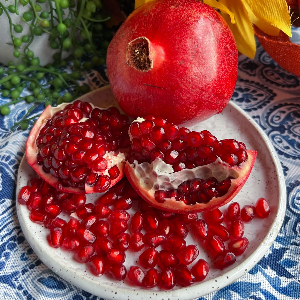 whole pomegranate, segmented pomegranate and pomegranate seeds on blue and white table cloth
