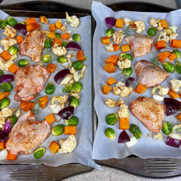 two sheet pans of fall veggies and skin on chicken thighs seasoned