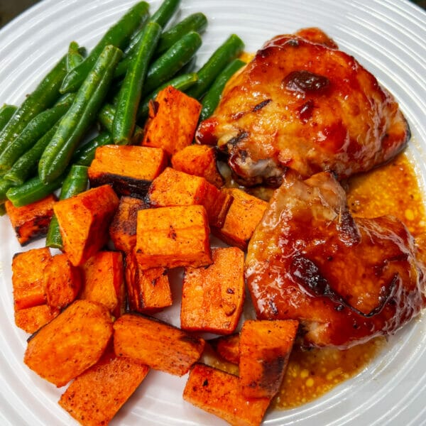 plate of sweet potatoes, green beans and two baked chicken thighs with cranberry molasses bbq sauce 

