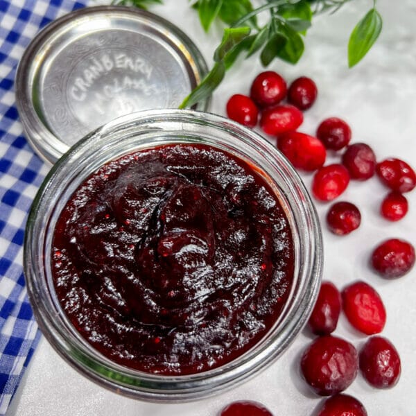 cranberry molasses bbq sauce in jar with lid on side and cranberries around it
