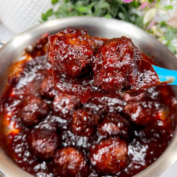 two meatballs covered in cranberry molasses bbq sauce on spoon over pot