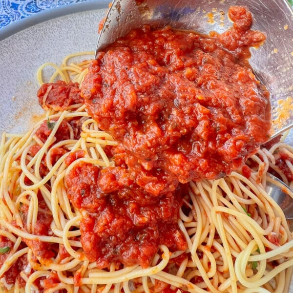 ladle pouring tomato sauce on spaghetti in bowl
