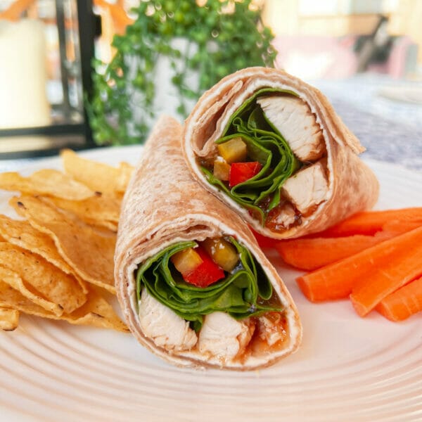 chicken and spinach wrap with hot pepper jelly on plate with carrots and tortilla chips
