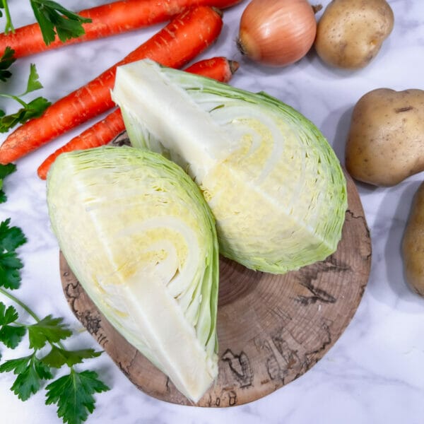 quartered green cabbage on counter with carrots and potatoes
