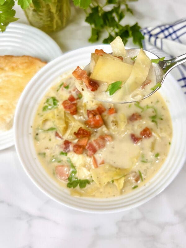 creamy cabbage soup in bowl with spoon showing biteful with potato and bacon
