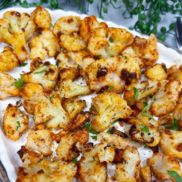 roasted, seasoned cauliflower and parsley pieces on a white platter
