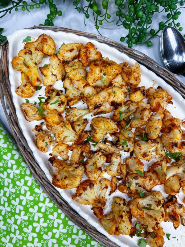 white platter with well seasoned oven roasted frozen cauliflower and a garnish of parsley
