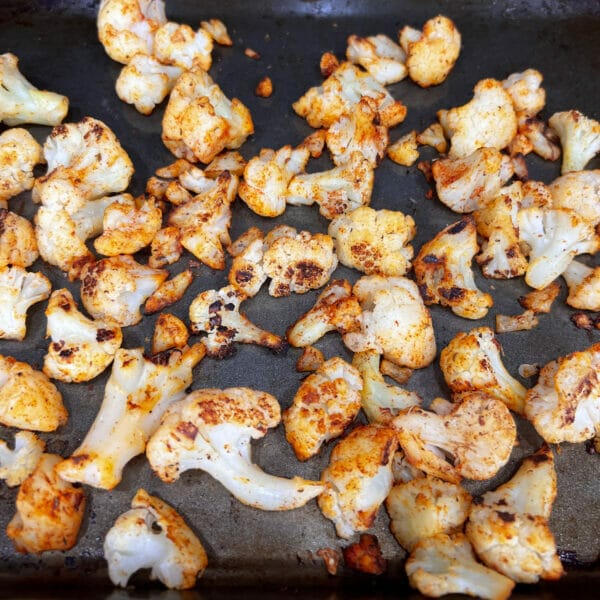 Seasoned cauliflower on baking sheet showing browning and some charring
