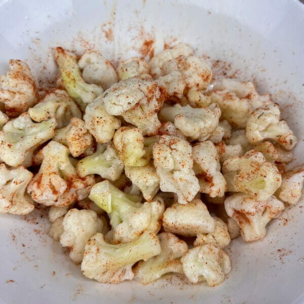 frozen cauliflower pieces in bowl tossed with oil and Cajun seasoning.

