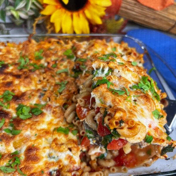 pan of macaroni chicken and spinach bake with one serving being taken out
