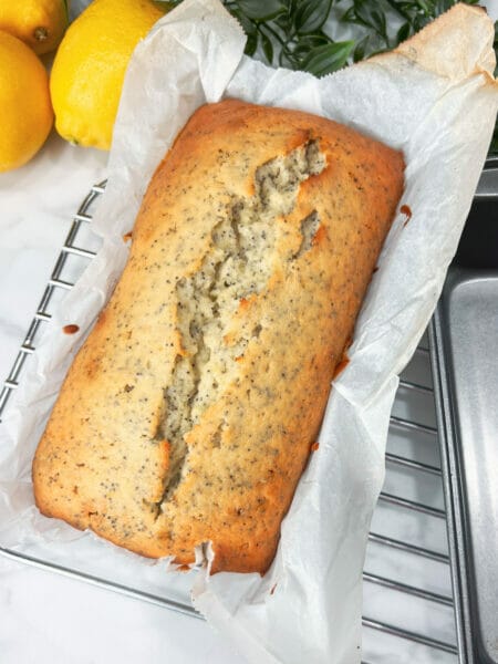 whole lemon poppyseed cake in parchment on a cooling rack
