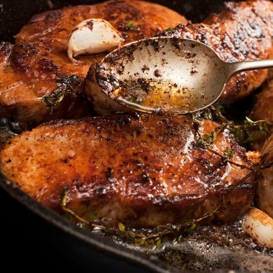 browned pork chops in cast iron pan drizzled with butter in spoon