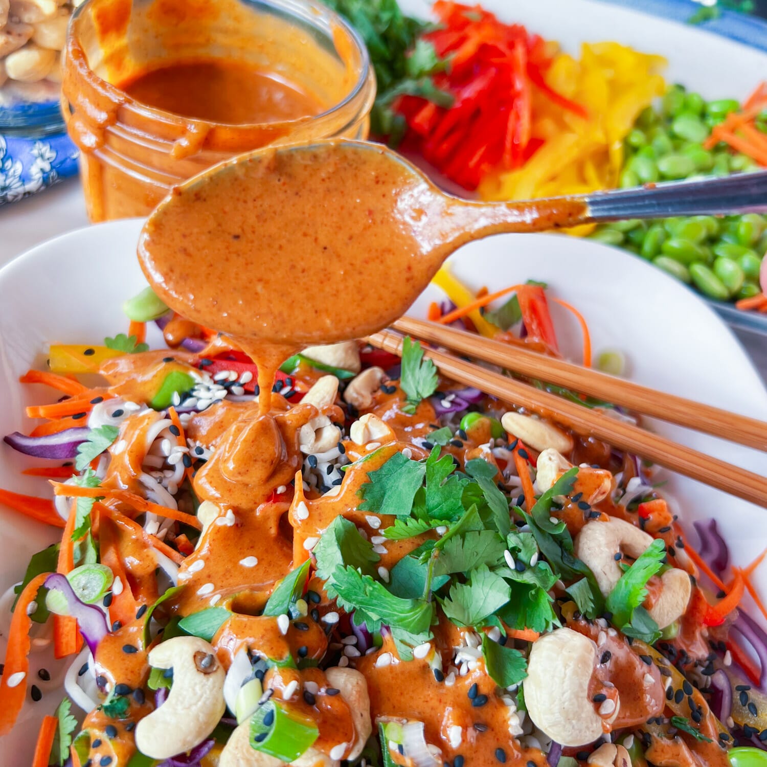 spoon of nut butter dressing over plate of thai power bowl ingredients 