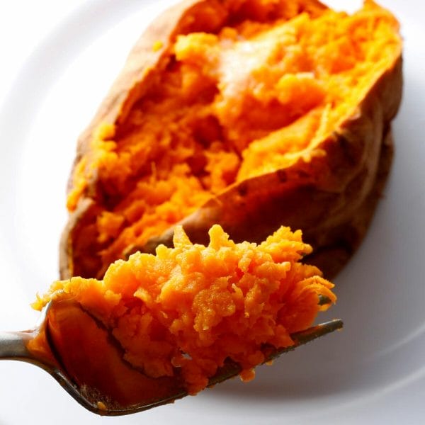 cooked sweet potato, sliced open and topped with butter. forkful of potato in close up