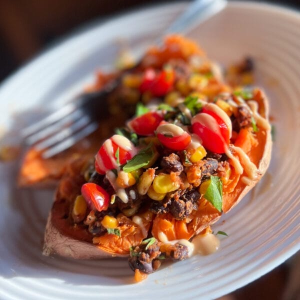sweet potato on plate stuffed with beans, corn garnished with tomatoes cilantro